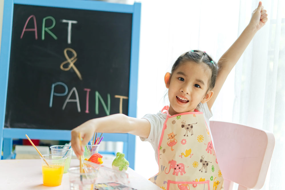 Preschool child smiling proudly while holding artwork, supported by a parent’s encouragement.