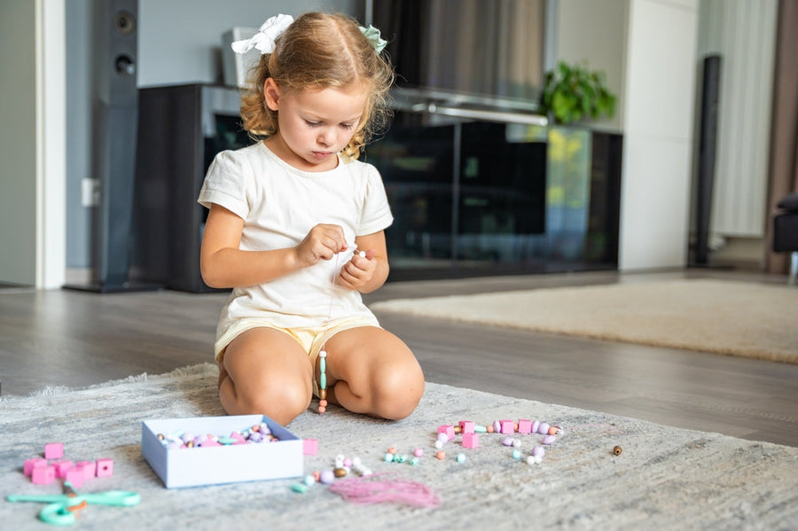Preschool child using thread and bead materials during hands-on fine motor activity.